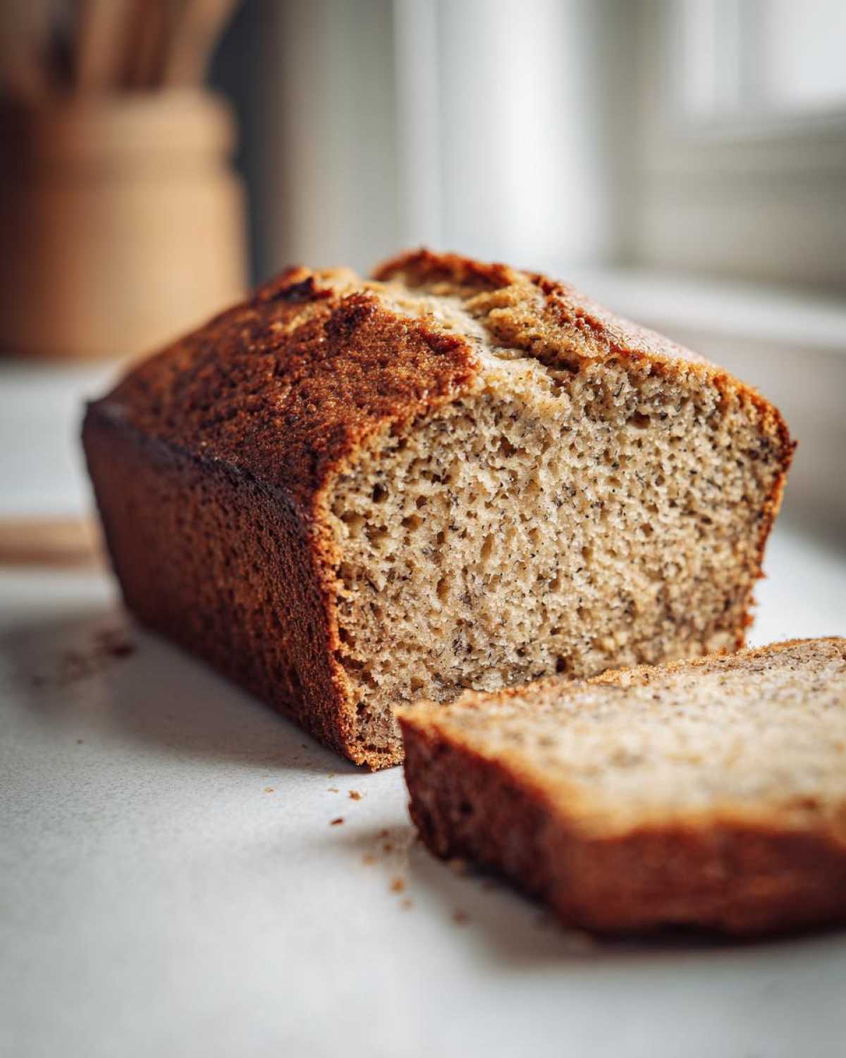 Close-up of a freshly baked greek yogurt banana bread loaf with one slice cut, showing the moist, speckled crumb.