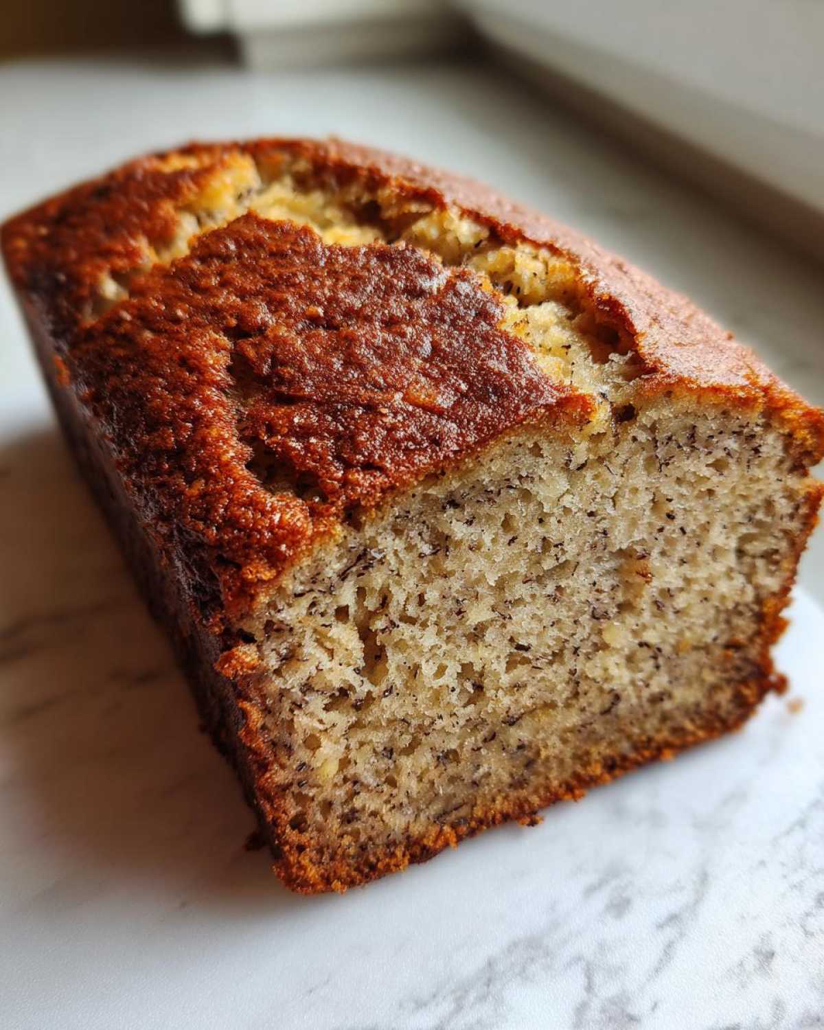 A close-up of a freshly baked loaf of greek yogurt banana bread showing the moist crumb and golden-brown crust.
