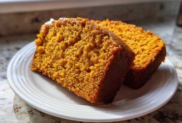 Two thick slices of moist, orange-colored pumpkin bread sitting on a white plate.