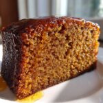 Close-up of a moist slice of dark brown rum cake recipe, dripping with shiny glaze.