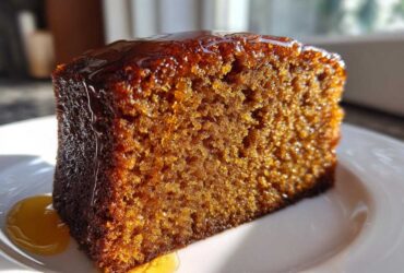 Close-up of a moist slice of dark brown rum cake recipe, dripping with shiny glaze.