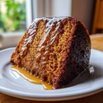 A close-up of a moist slice of rum cake recipe, heavily drizzled with a rich, glossy caramel glaze.