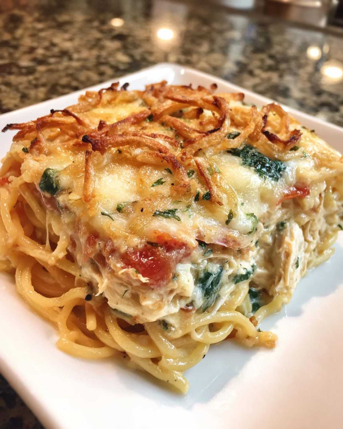 A square serving of creamy monterey chicken spaghetti topped with melted cheese and crispy onions.