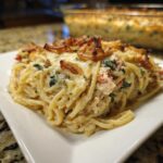 A close-up serving of creamy monterey chicken spaghetti casserole topped with crispy fried onions.