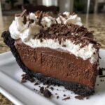 A perfect slice of no-bake chocolate mousse pie with a dark crust, topped with whipped cream and chocolate shavings.