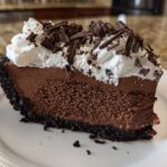 A rich slice of no-bake chocolate mousse pie with a dark crust, topped with whipped cream and chocolate shavings.