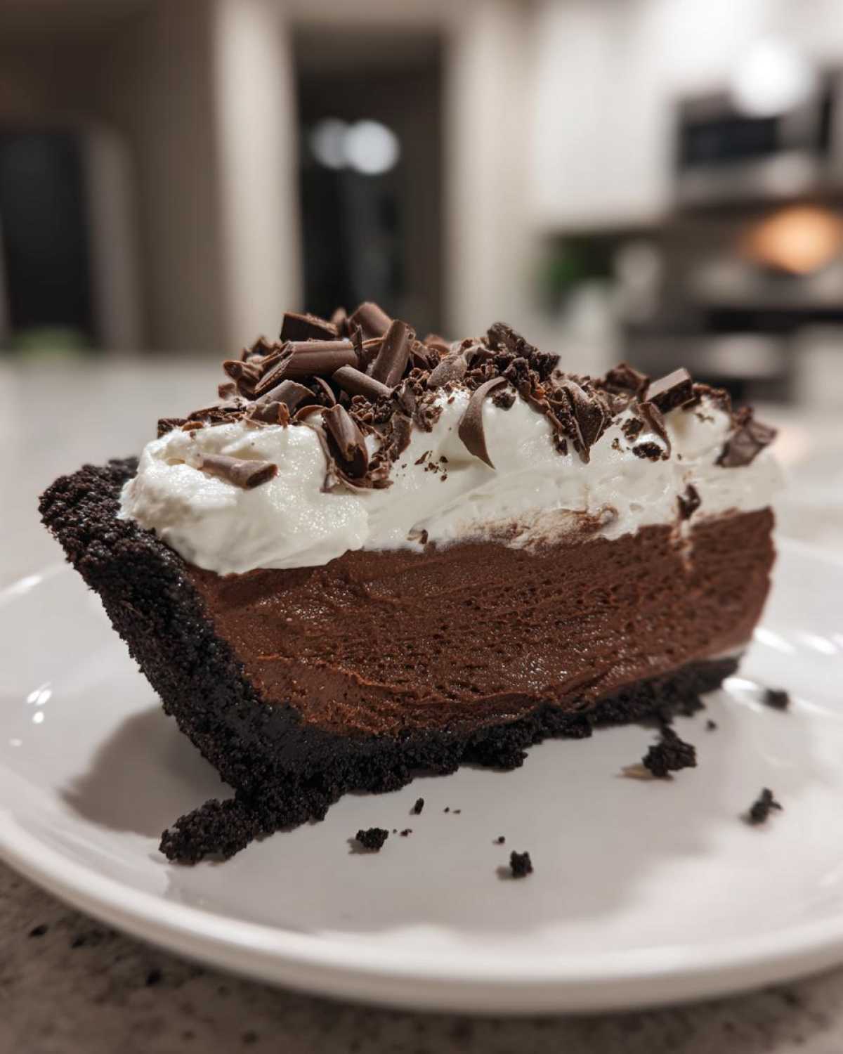 A decadent slice of no-bake chocolate mousse pie featuring a dark crust, rich filling, whipped cream, and chocolate shavings.