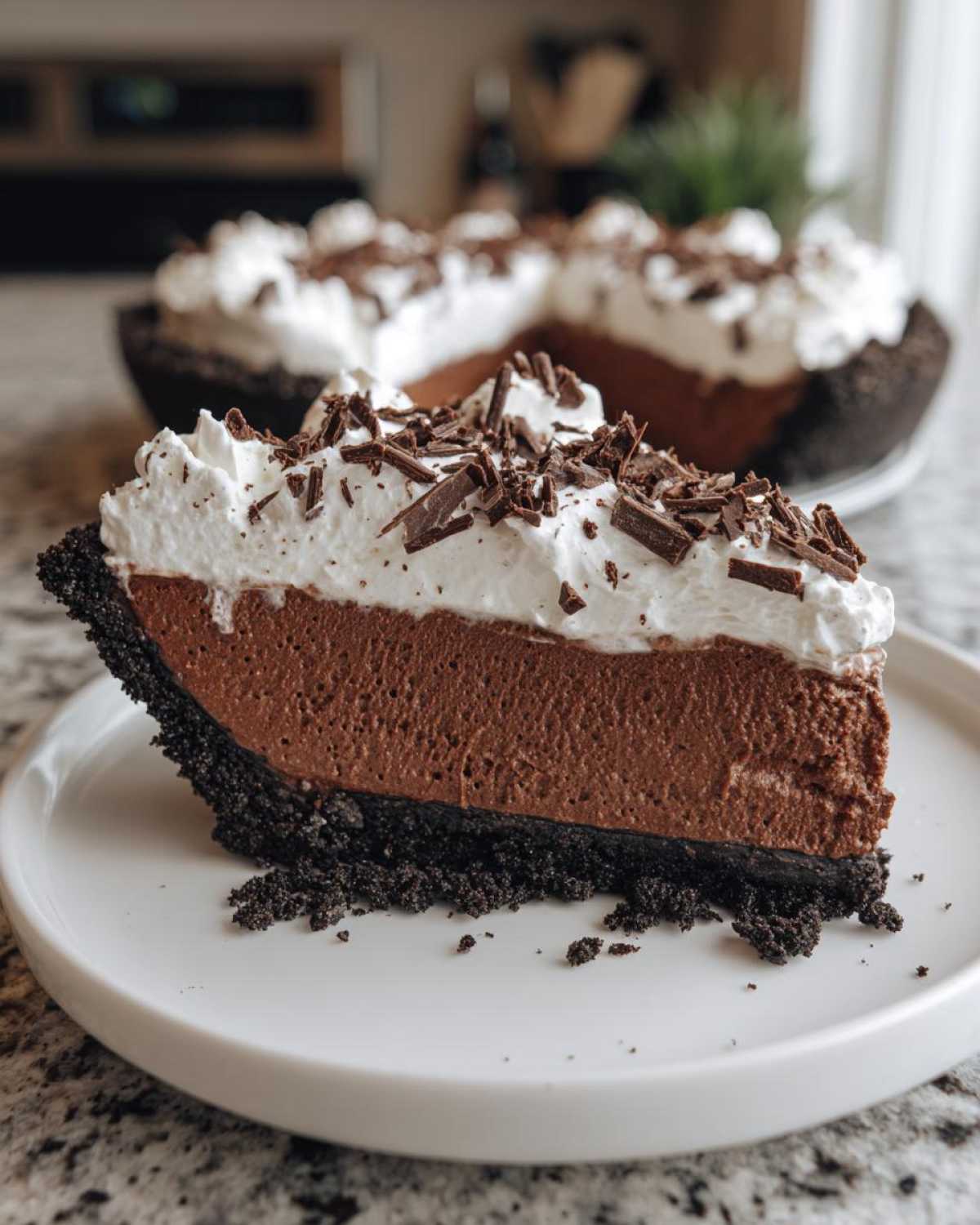 A close-up of a rich slice of no-bake chocolate mousse pie with whipped cream and chocolate shavings.