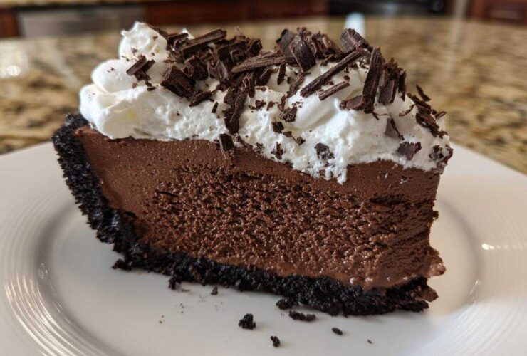 A rich slice of no-bake chocolate mousse pie with a dark crust, topped with whipped cream and chocolate shavings.