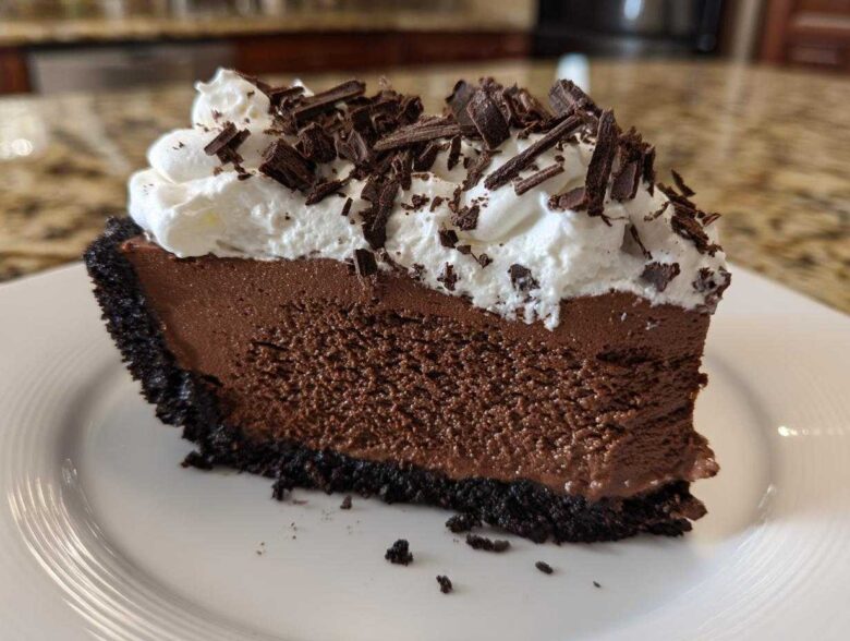 A rich slice of no-bake chocolate mousse pie with a dark crust, topped with whipped cream and chocolate shavings.