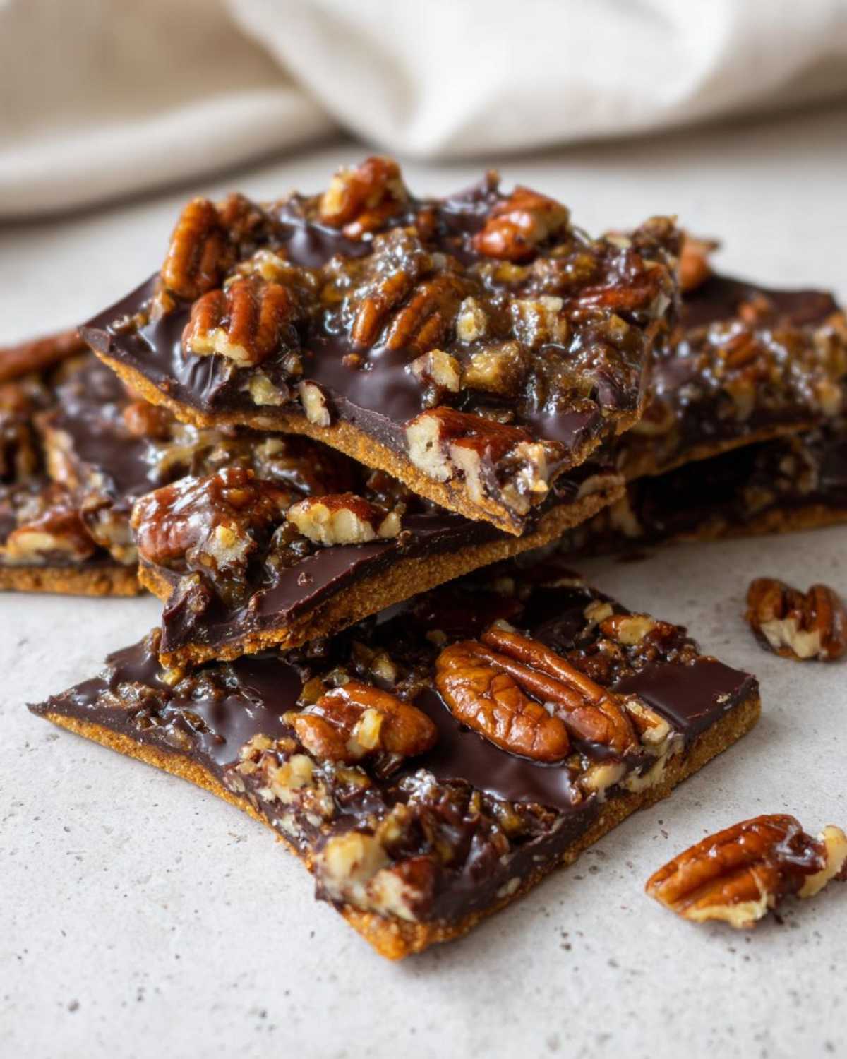 Close-up of stacked squares of rich Pecan Pie Bark featuring a chocolate layer and candied pecans.