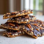 A stack of rich, dark chocolate Pecan Pie Bark pieces topped with whole and chopped pecans.