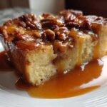 A close-up of a square slice of pecan pie bread pudding drenched in rich caramel sauce.