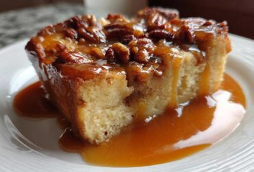 A close-up of a square slice of pecan pie bread pudding drenched in rich caramel sauce.