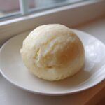 A smooth, round ball of homemade fufu served on a small white plate near a window.