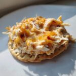 Close-up of a cracker topped with warm, cheesy Reuben dip, showing shredded texture and melted orange cheese.