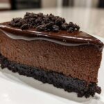 A decadent slice of rich chocolate cheesecake with a dark cookie crust, glossy chocolate ganache, and crumbled topping.