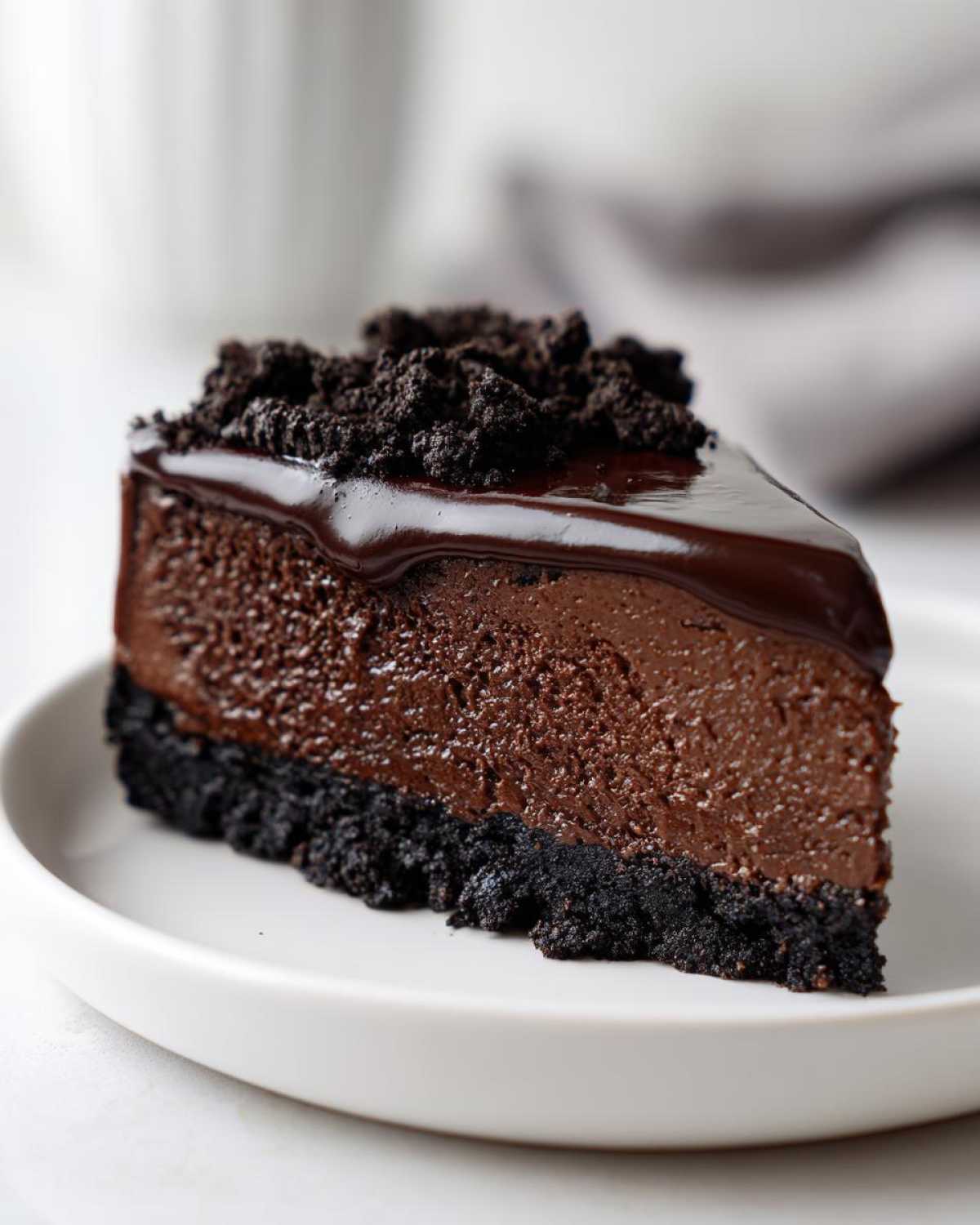A perfect slice of rich chocolate cheesecake with a dark cookie crust, topped with chocolate ganache and crumbles.