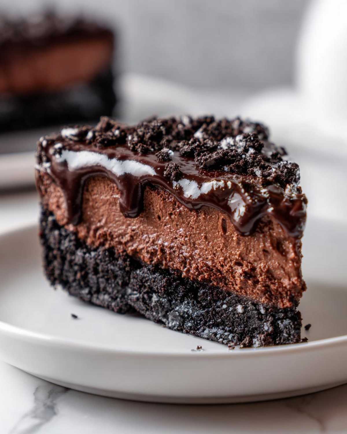 A decadent slice of chocolate cheesecake with a dark cookie crust, creamy filling, chocolate ganache, and cookie crumbs.