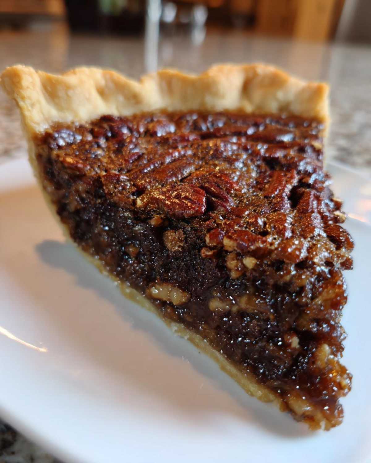 A close-up of a thick slice of chocolate pecan pie showing the gooey filling and pecan topping on a white plate.