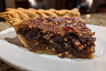 Close-up of a rich slice of chocolate pecan pie showing the flaky crust and gooey filling.