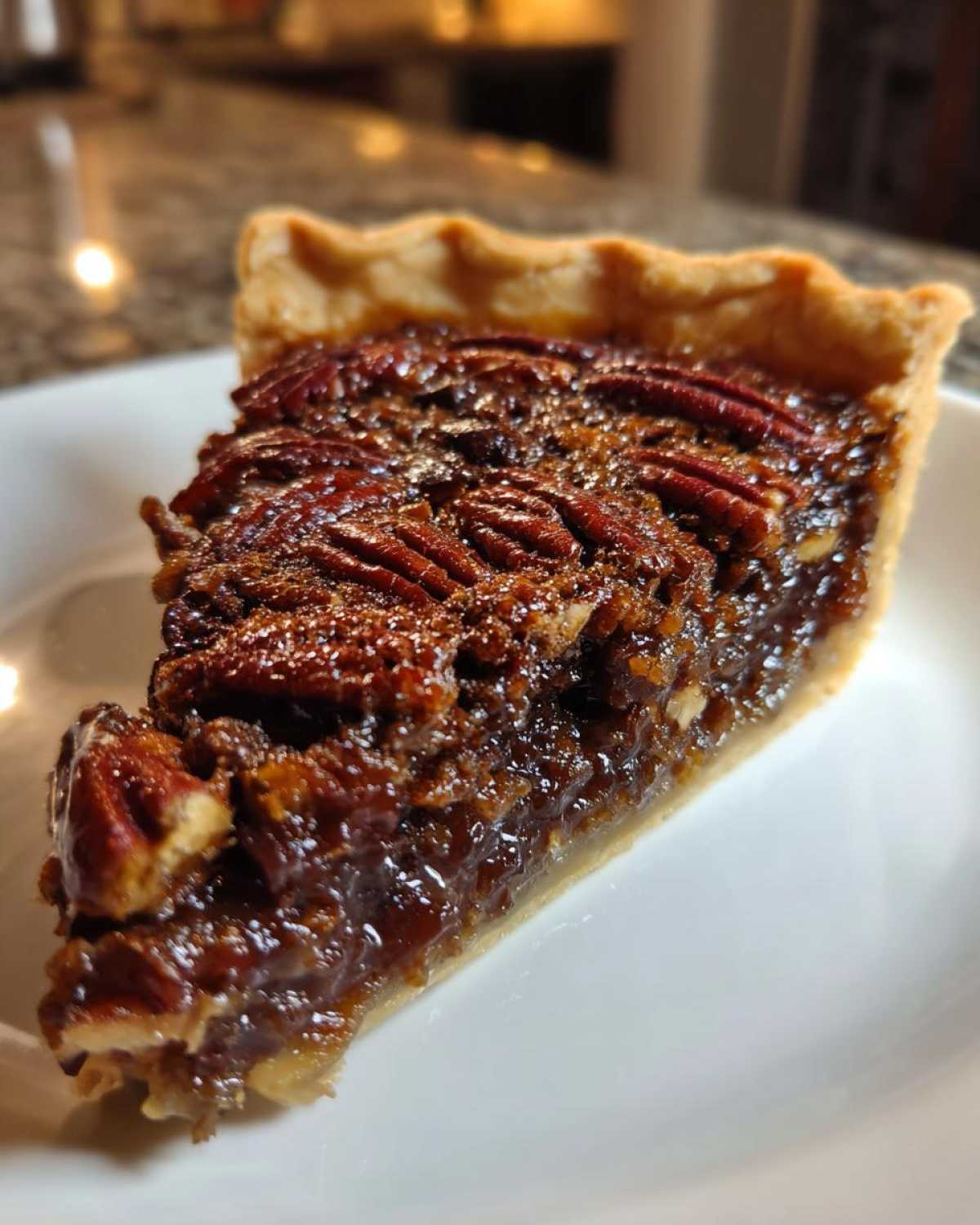 Close-up of a glistening slice of chocolate pecan pie showing the rich filling and whole pecans on top.