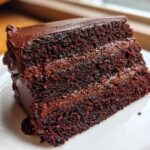 Close-up of a moist slice of homemade chocolate cake with dark chocolate frosting layers.