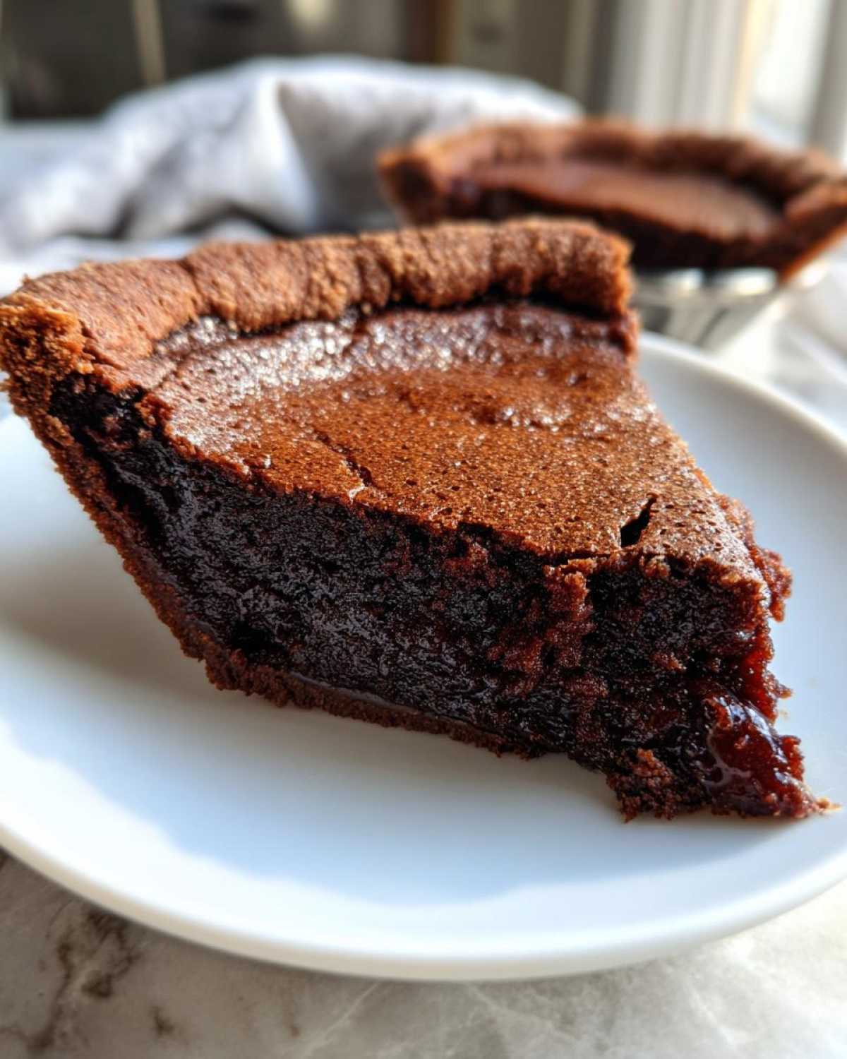 Close-up of a decadent slice of fudge pie showing a dark, molten center on a white plate.