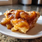 Close-up of a slice of pie showing thick, glossy apple pie filling loaded with cinnamon spices.