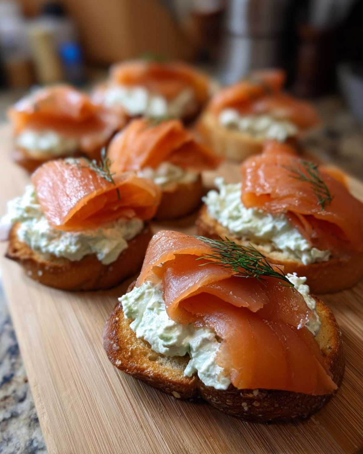 Close-up of several smoked salmon bites topped with herbed cream cheese on toasted bread slices.