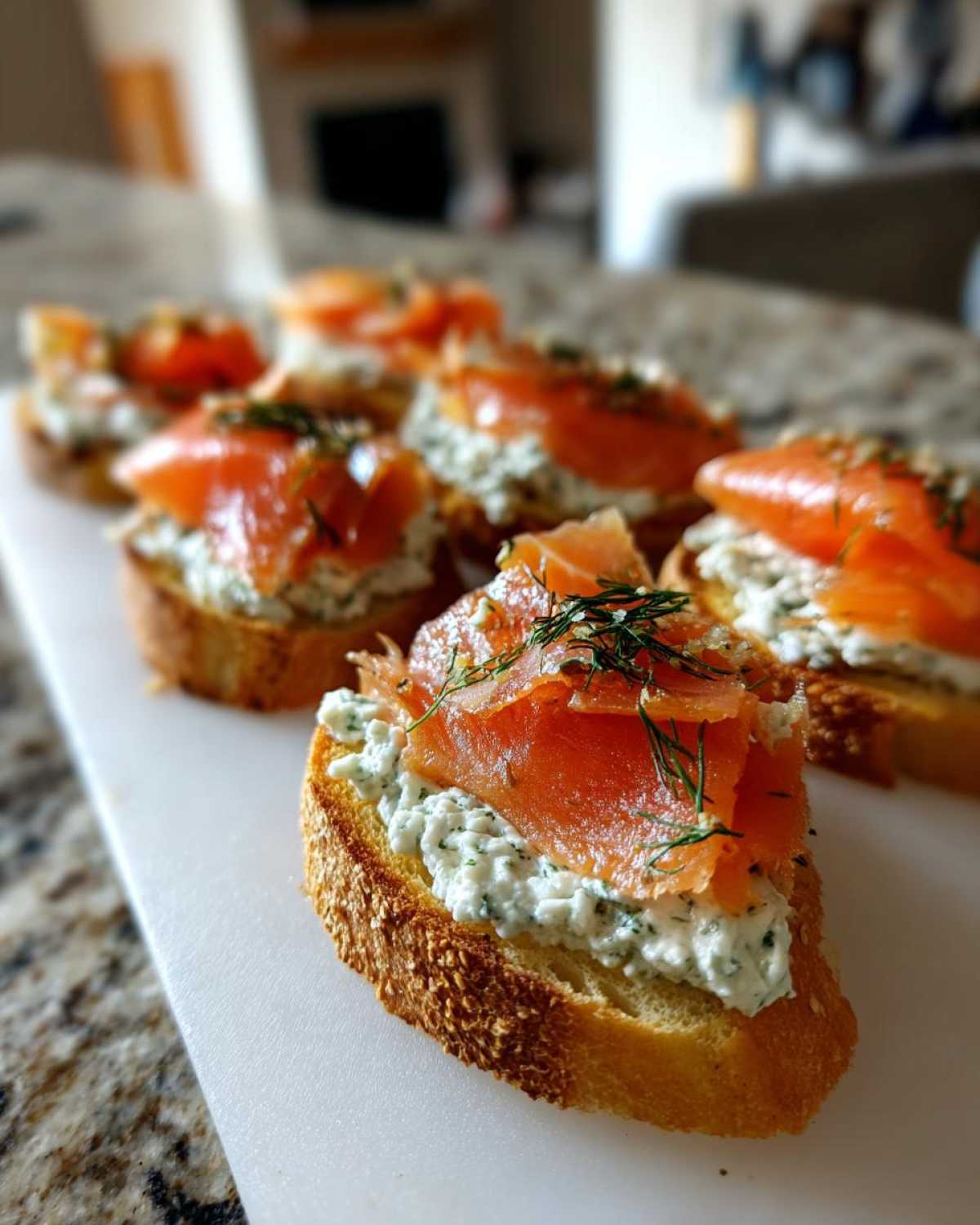 Close-up of several smoked salmon bites served on toasted bread with creamy herb cheese and fresh dill.