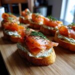 Close-up of several smoked salmon bites on toasted bread with dill cream cheese, garnished with fresh dill.