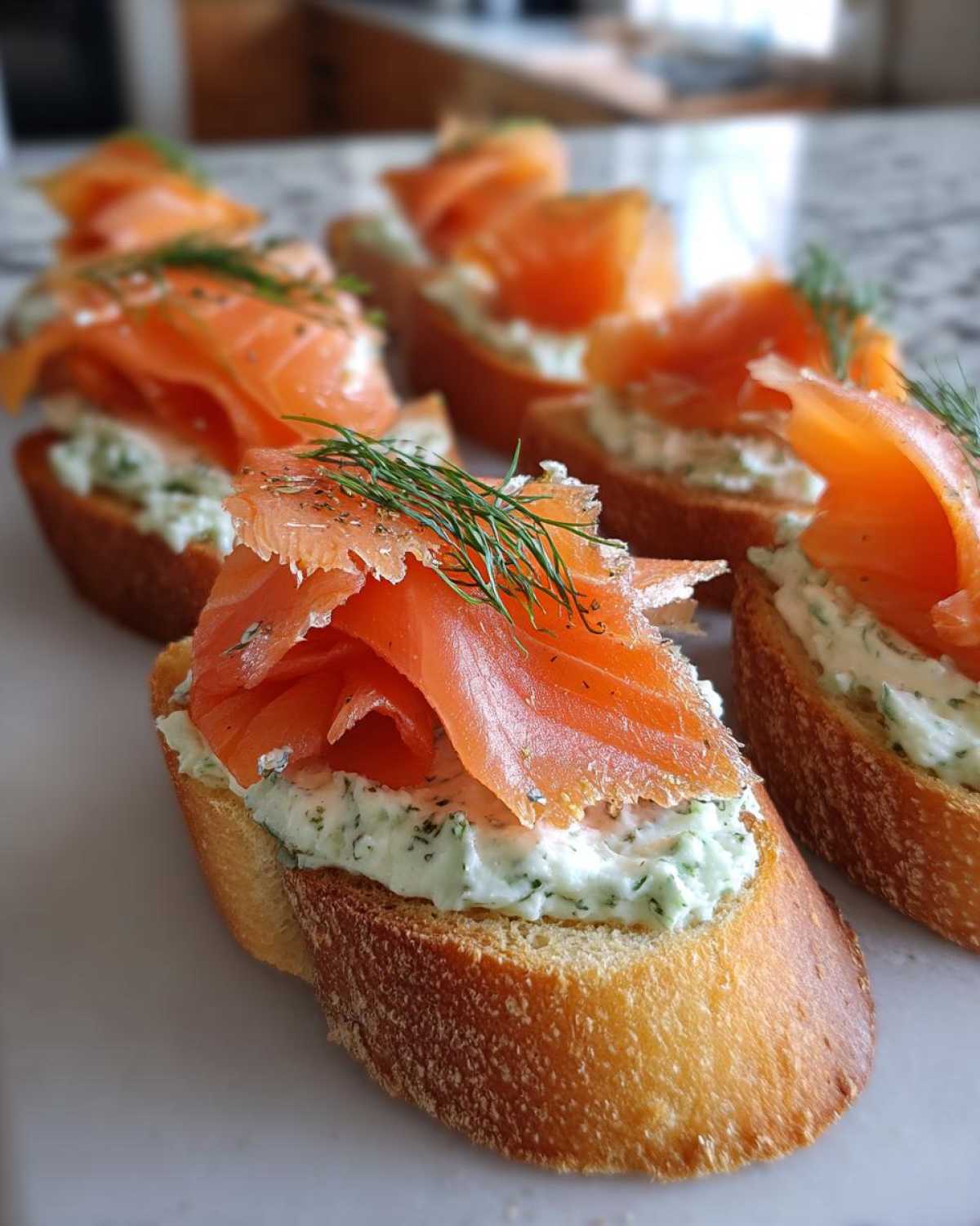 Close-up of several smoked salmon bites on toasted baguette slices topped with dill cream cheese.