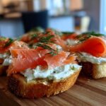 Close-up of several smoked salmon bites served on toasted bread with cream cheese and fresh dill garnish.