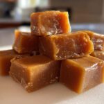 Close-up of a small pile of soft, golden brown homemade caramel squares glistening in the light.