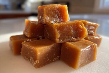 Close-up of a small pile of soft, golden brown homemade caramel squares glistening in the light.