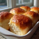 Six golden brown, glossy sourdough discard rolls baked together in a white dish.