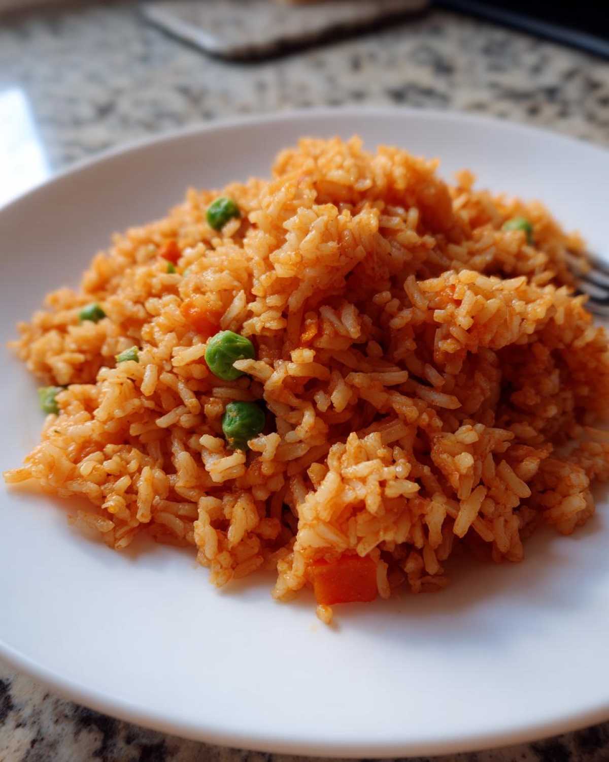 A close-up of a serving of vibrant orange Spanish rice mixed with green peas on a white plate.