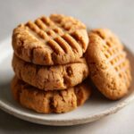 A close-up stack of four golden brown peanut butter cookies featuring classic criss-cross fork marks.