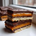Two stacked homemade twix cookies showing a shortbread base, thick caramel, and dark chocolate topping.