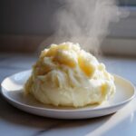 A generous mound of fluffy, steaming hot mashed potatoes served on a white plate.