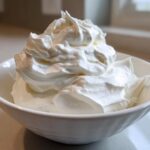 Close-up of stiff, bright white peaks of icing mixture in a white bowl, representing the royal icing recipe.