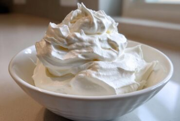 Close-up of stiff, bright white peaks of icing mixture in a white bowl, representing the royal icing recipe.