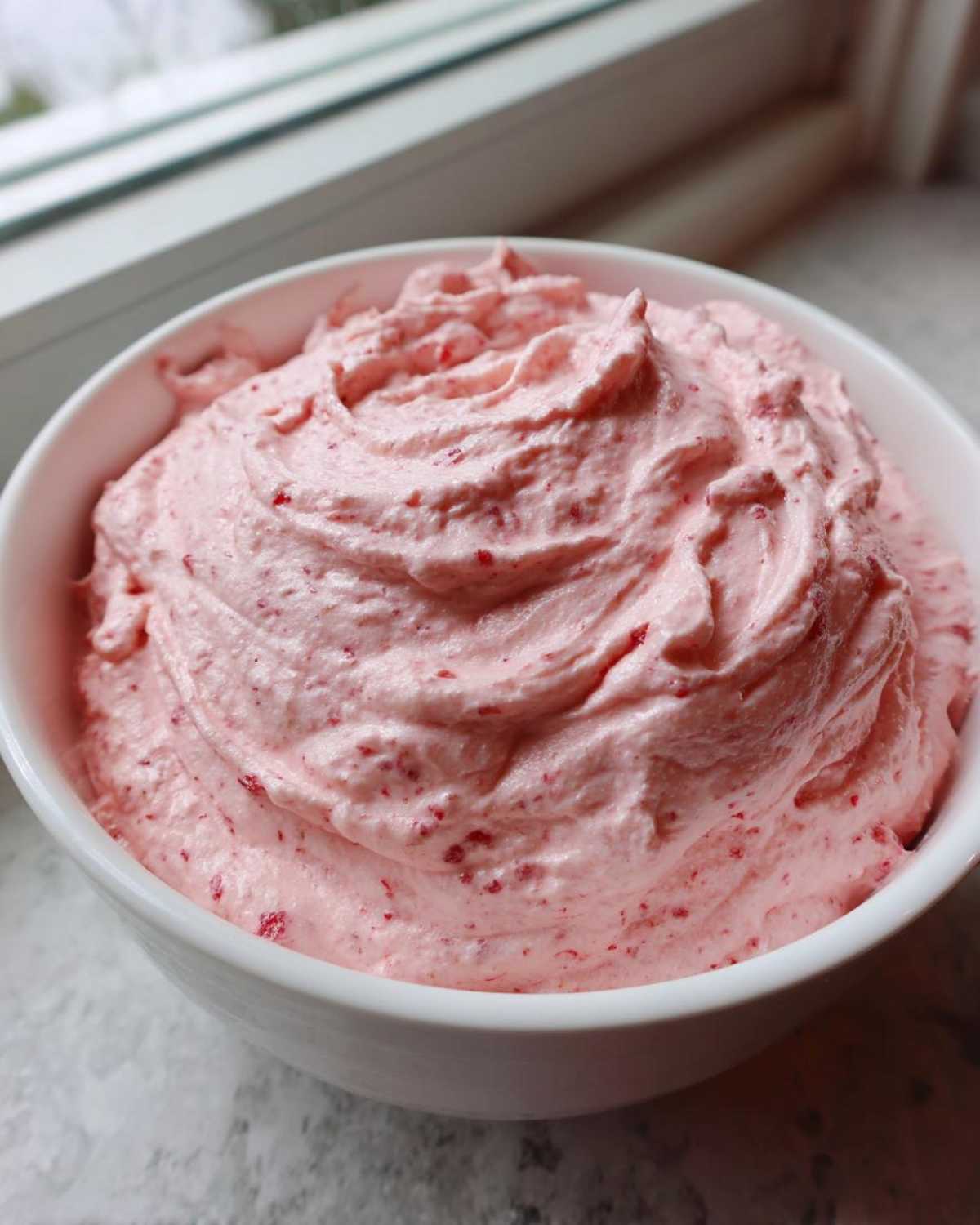 Close-up of fluffy, pink strawberry cheesecake dip swirled high in a white bowl.