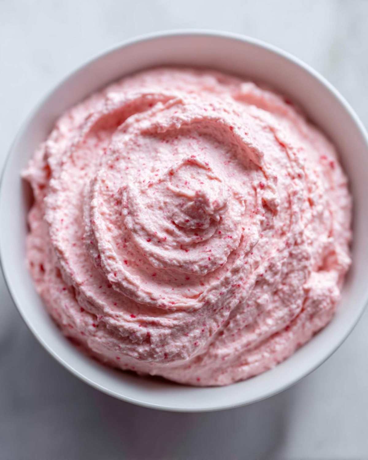 Close-up overhead view of creamy, pink strawberry cheesecake dip swirled in a white bowl.