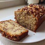 A loaf of sweet Alabama pecan bread sliced open on a white plate, showing a moist interior and pecan topping.