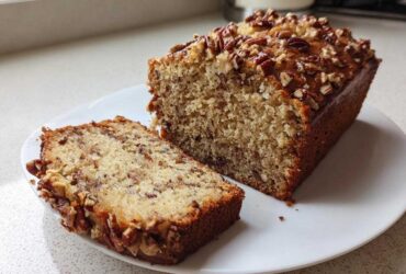 A loaf of sweet Alabama pecan bread sliced open on a white plate, showing a moist interior and pecan topping.