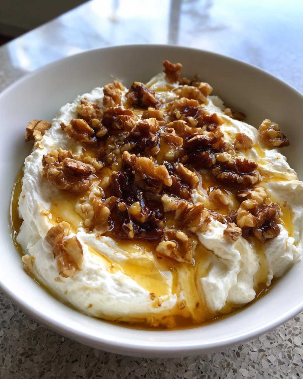 Close-up of a bowl of sweet whipped ricotta dip topped with candied walnuts and drizzled honey.