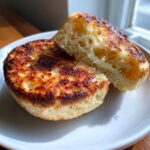 A toasted english muffin cut in half, showing its airy, hole-filled interior and golden-brown crust.