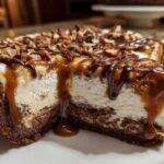 Close-up of a slice of turtle cheesecake showing the creamy filling, chocolate crust, and dripping caramel and chocolate sauce.